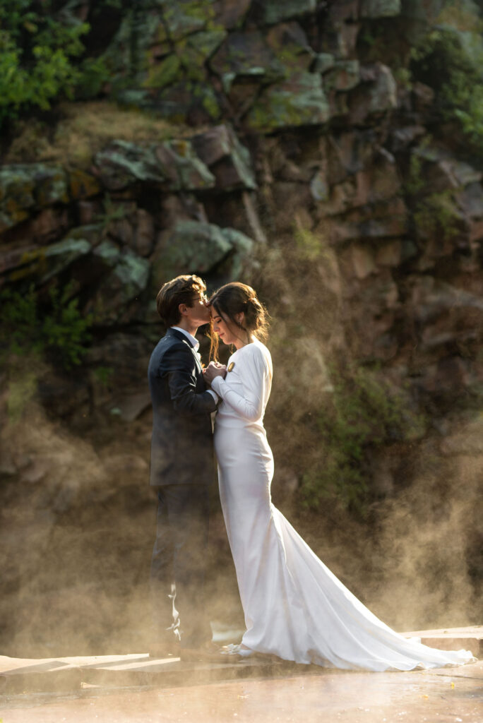 bride and groom stand in front of rock face with steam surrounded, during colorado micro wedding.