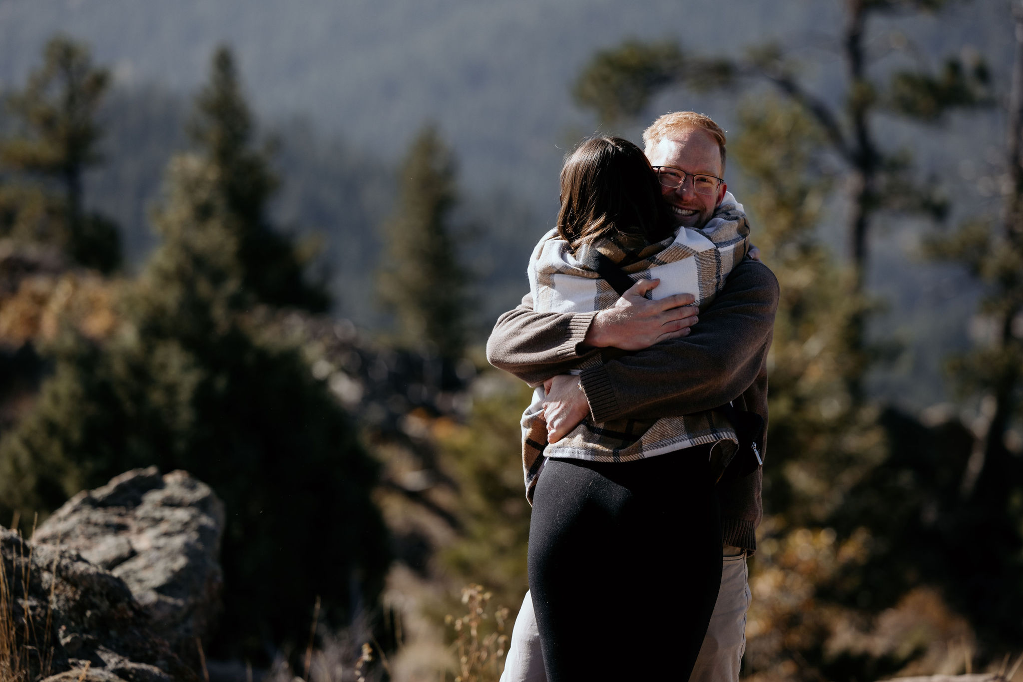 woman jumps into mans arms after he proposes to her in the mountains.