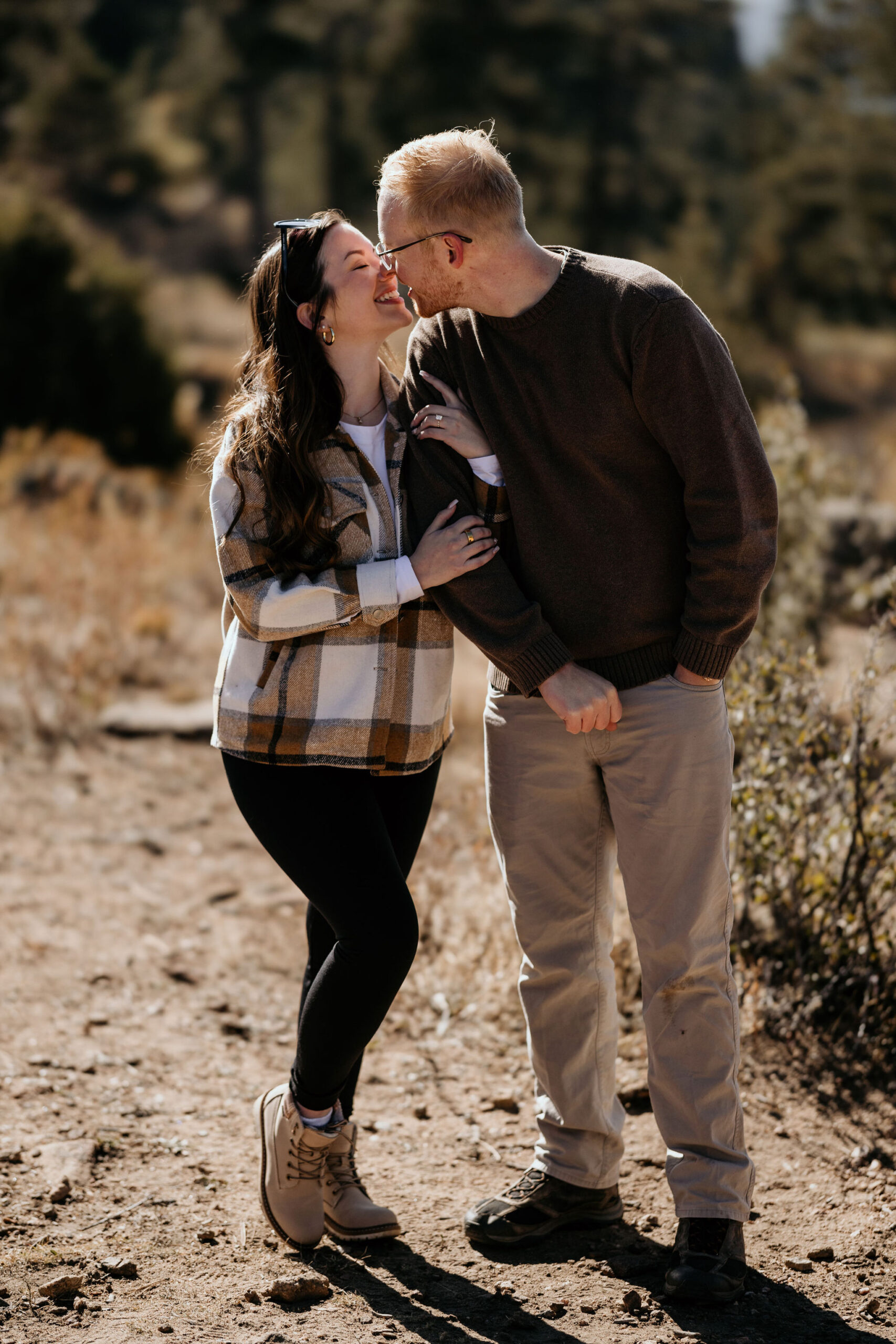 mand and woman smile and go in for a kiss in the colorado mountains after proposal.