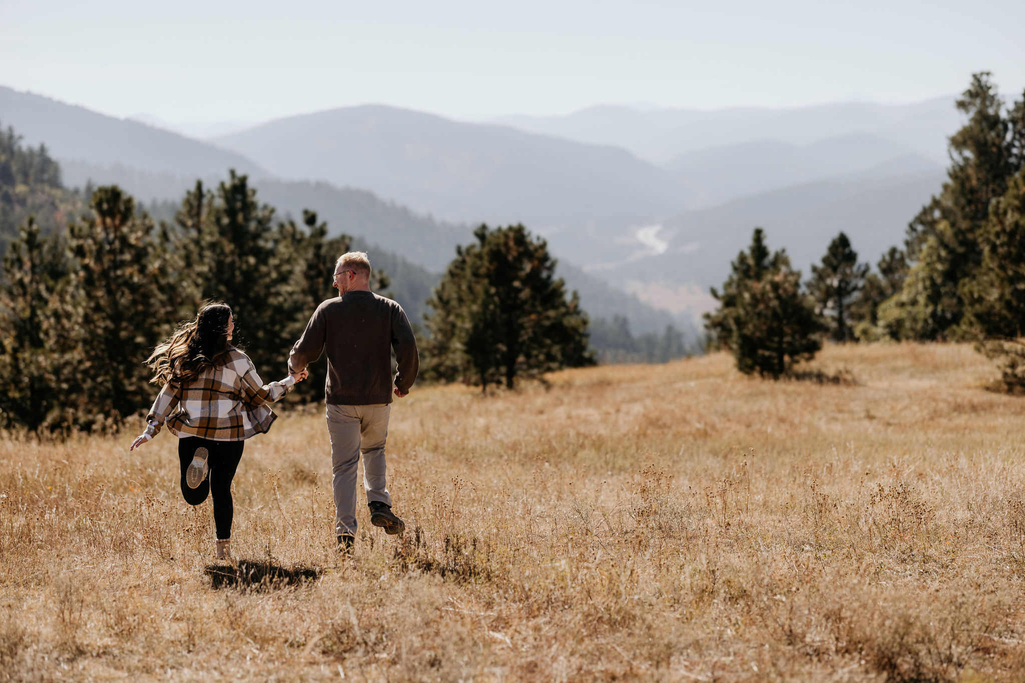 mand and woman hold hands and run towards the colorado mountains after their mountain proposal.
