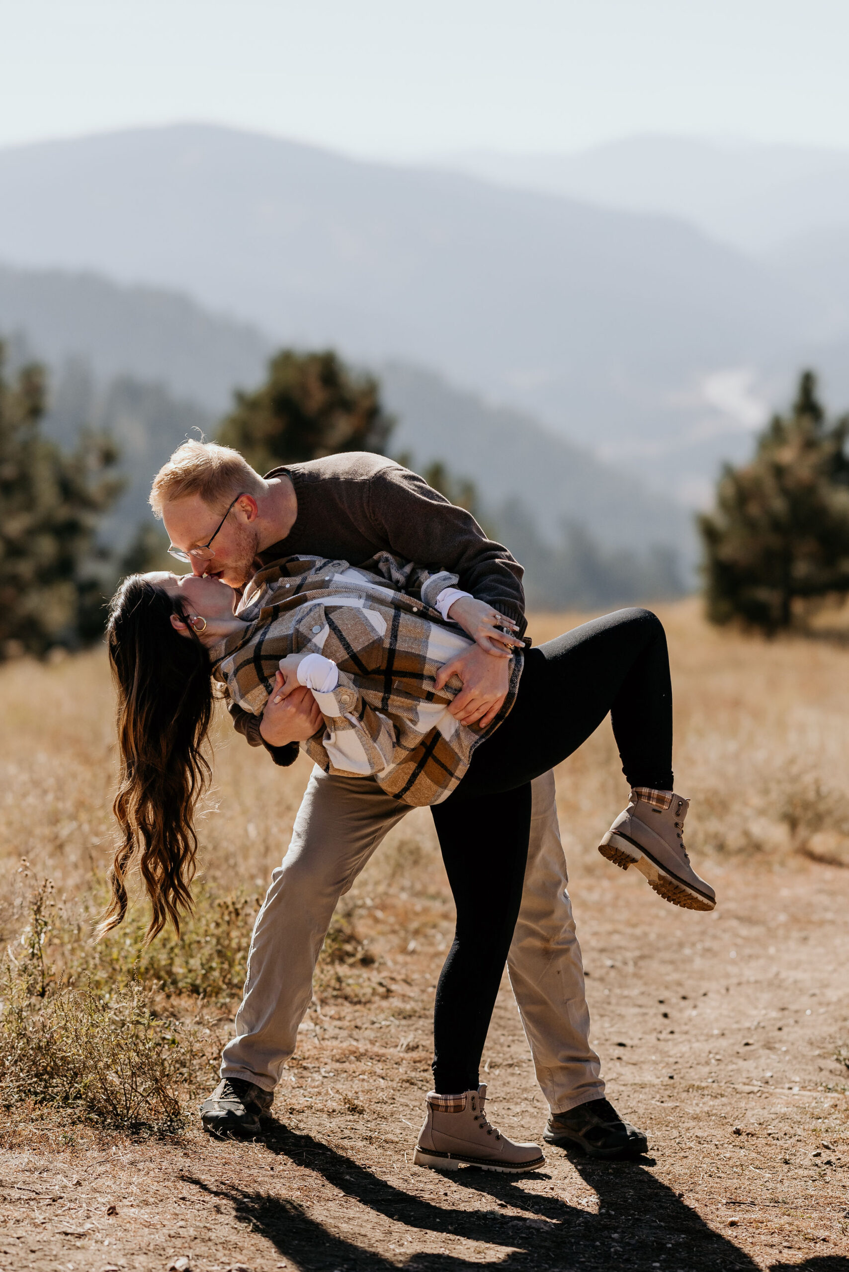 man dips woman and kisses her during their colorado engagement photos in the mountains.