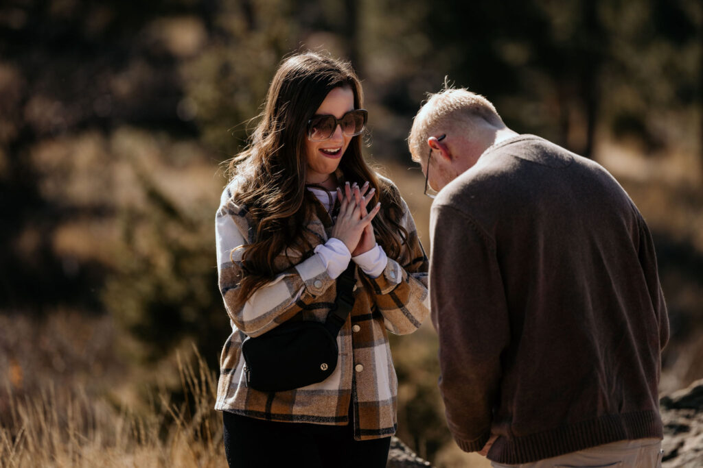 woman smiles as man is about to get down on one knee to propose in the colorado mountains.