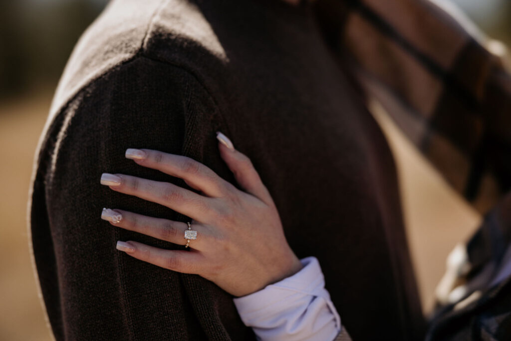 close up image of womans hand with engagement ring on her fiancees arm.