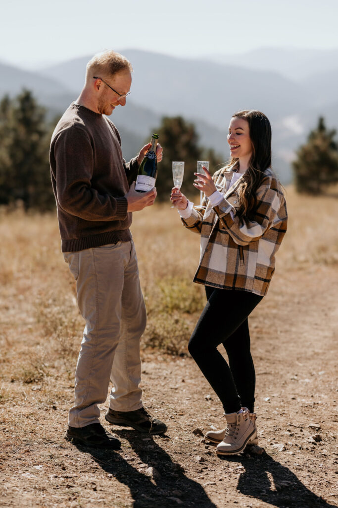 man and woman pour glasses of champagne during surprise colorado mountain proposal.