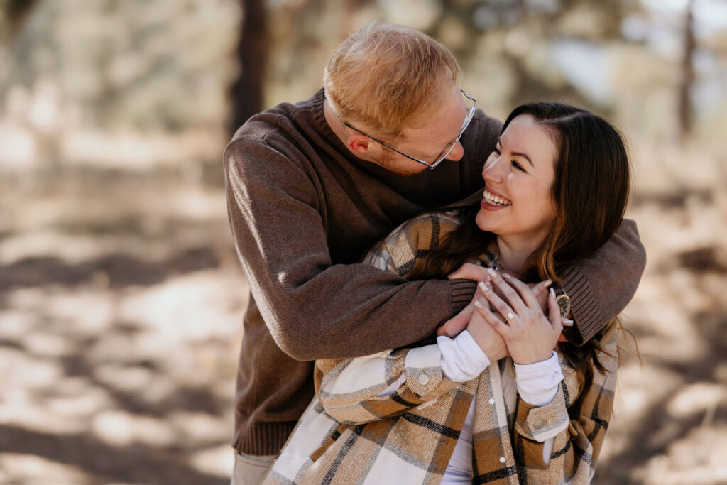 man puts arms around womans shoulders after their surprise proposal in the colorado mountains.