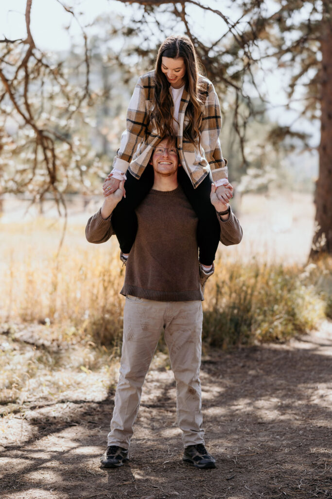 woman sits on mans shoulders during engagement photos.