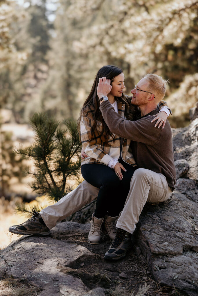 man tucks hair behind womans ear as they sit on a rock after their colorado mountain proposal.