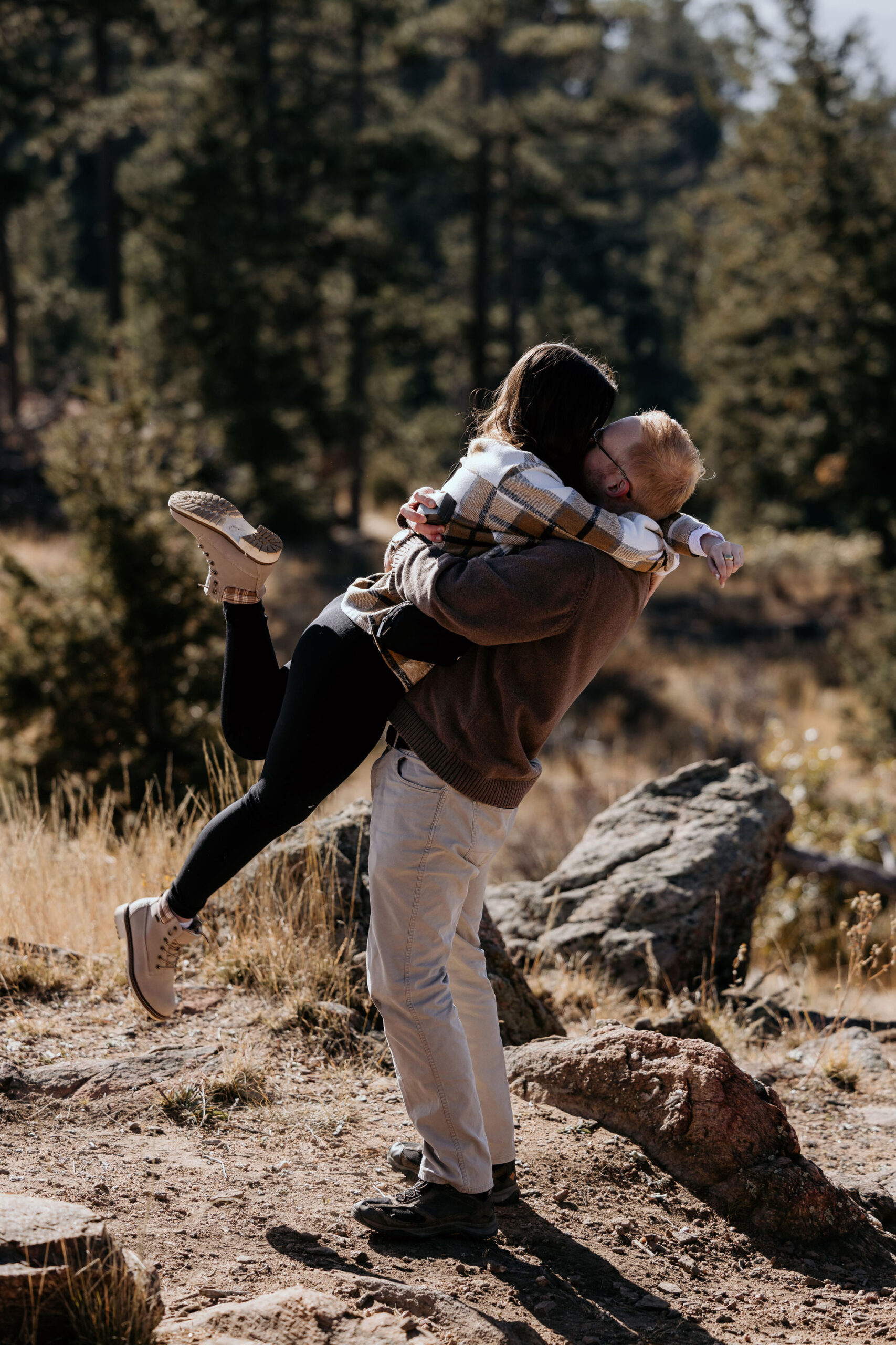 woman jumps into mans arms and kisses him after their surprise proposal in the mountains.