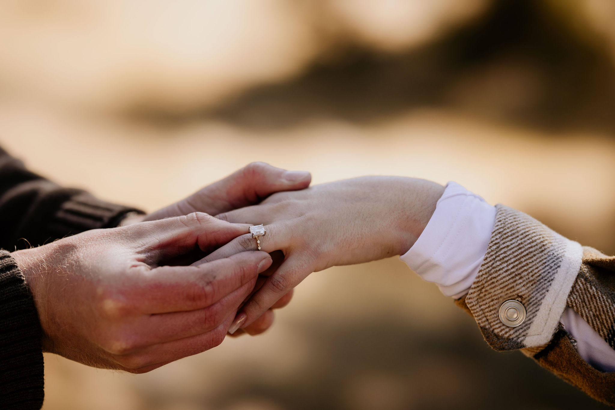 close up image of a man putting a ring on a womans finger during a surprise mountain proposal.
