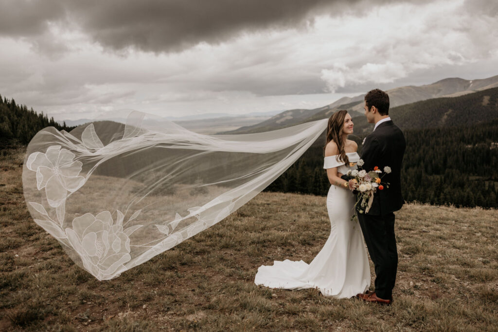 bride and groom stand in front of colorado mountains and face each other.