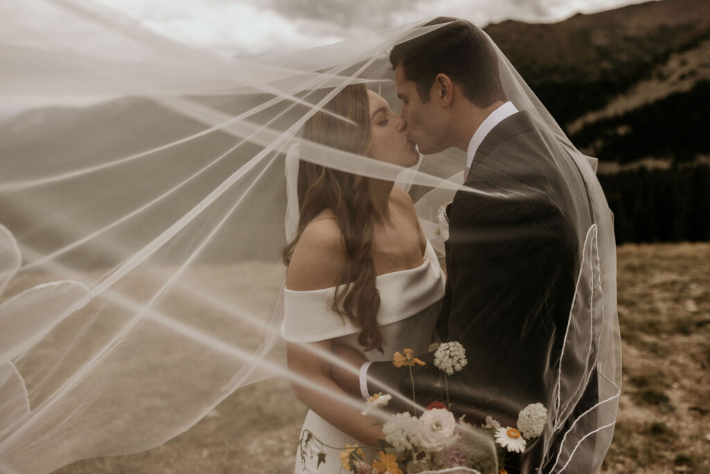bride and groom kiss under bride's veil during mountain wedding in Colorado.