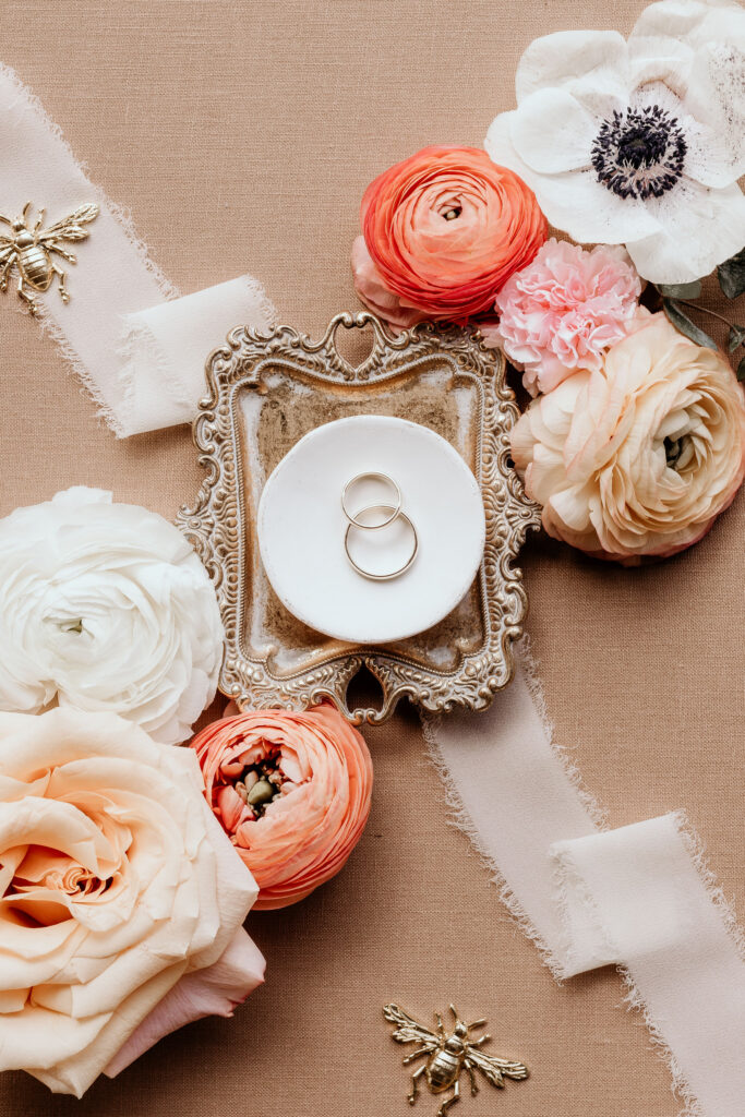 close up image of wedding rings on a small tray and florals.