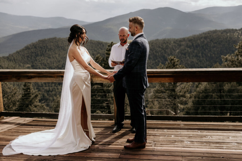 bride and groom stand on deck of airbnb with the colorado mountains behind.