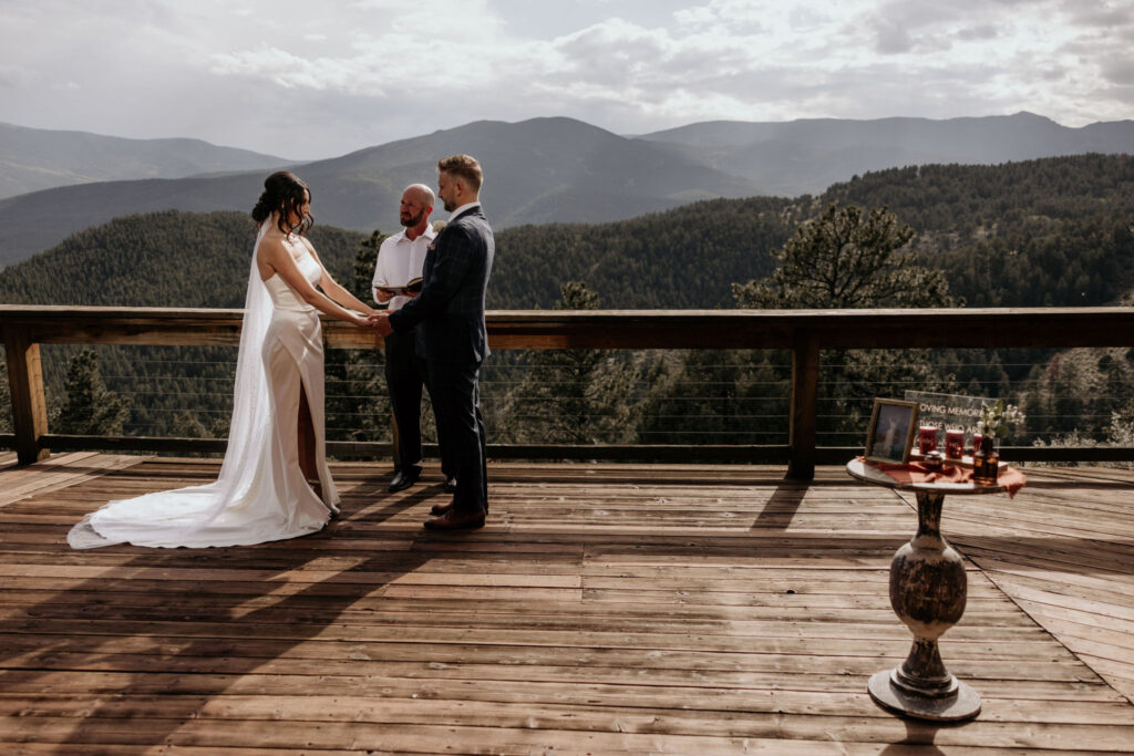 bride and groom stand at wedding ceremony with memorial table beside them, mountain views in the background.