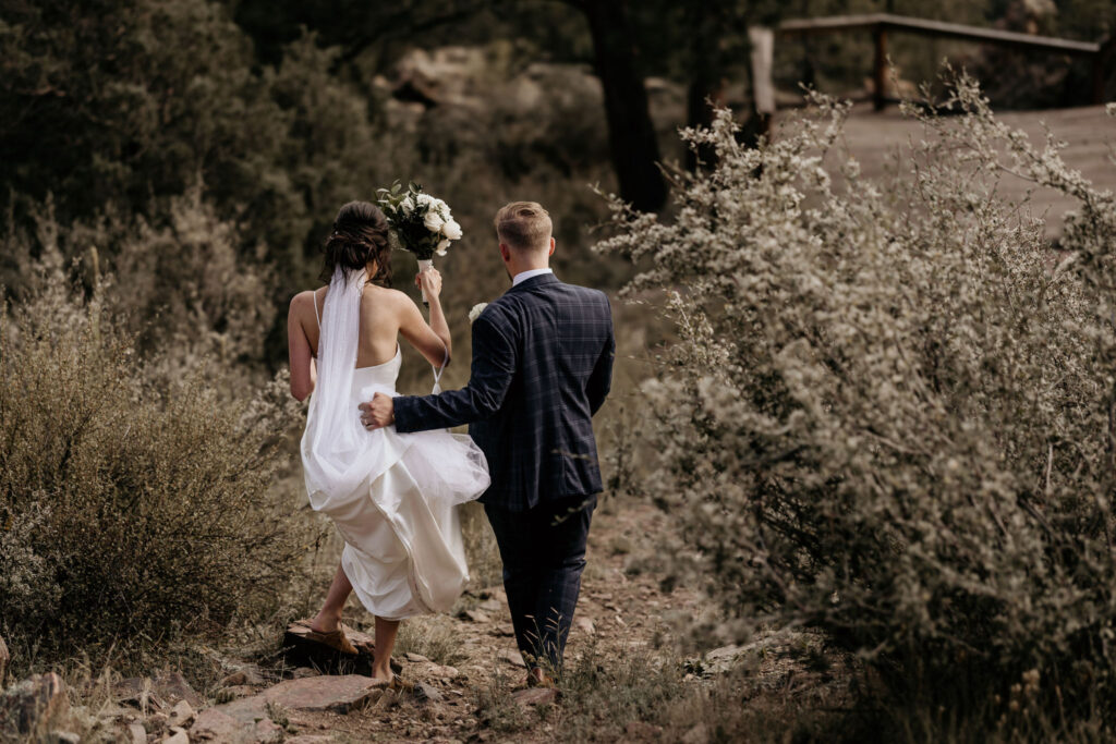 bride and groom wlak down trail during wedding portraits.
