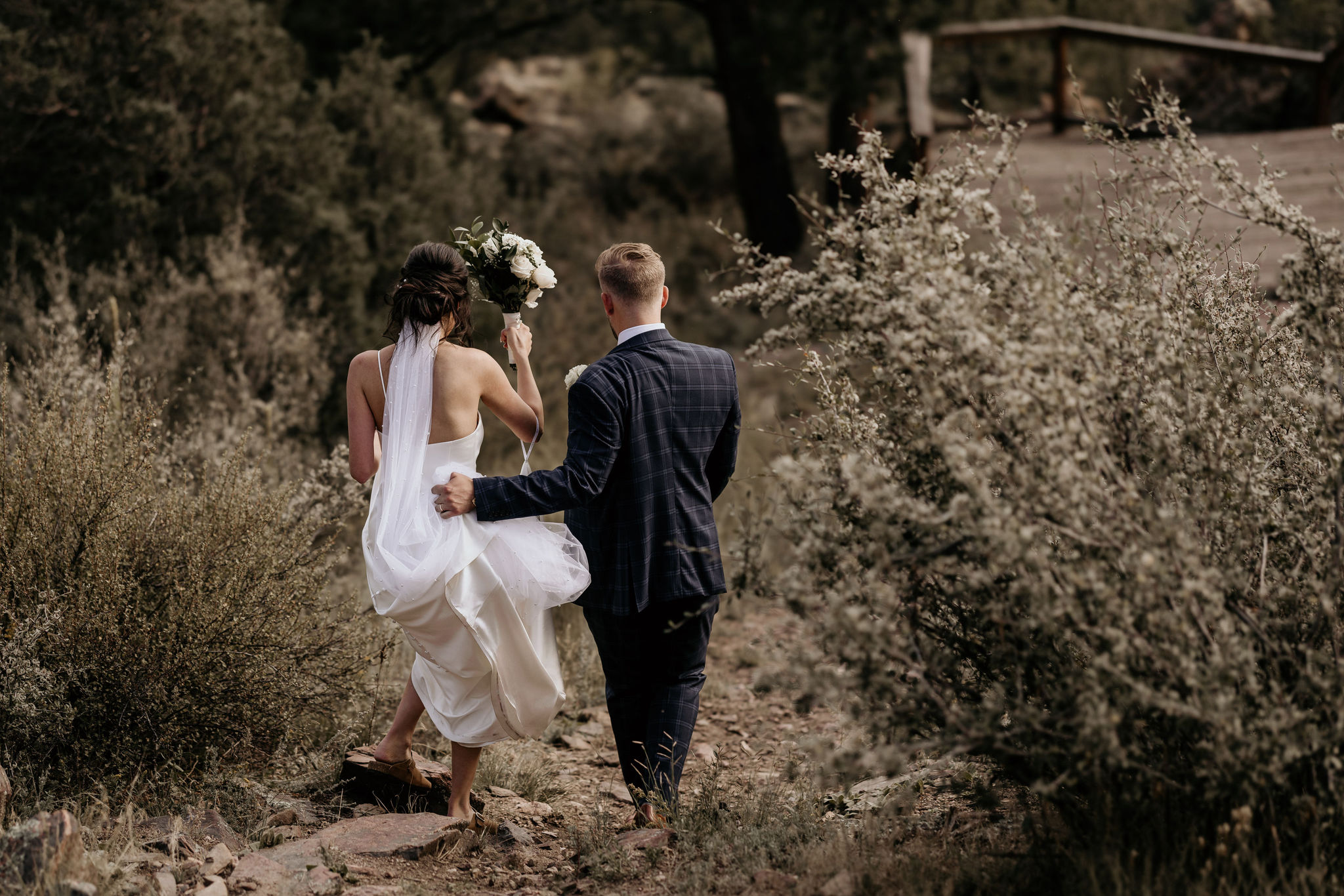 bride and groom walk down trail during wedding portraits in colorado
