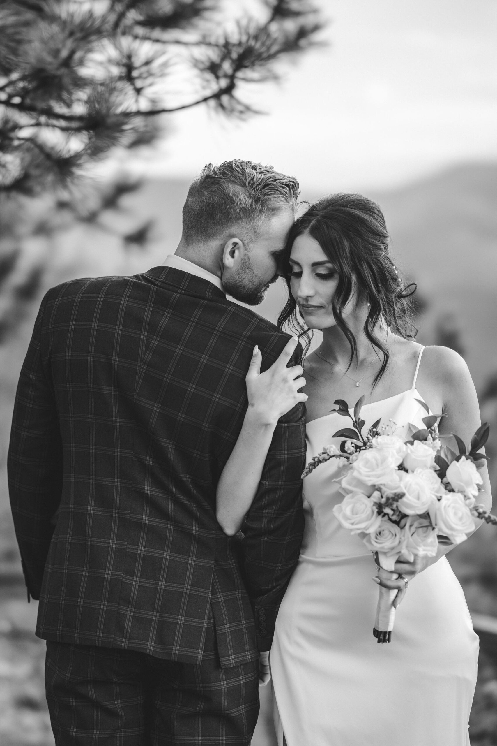 bride wraps arm around grooms arm and press heads together during wedding portraits.