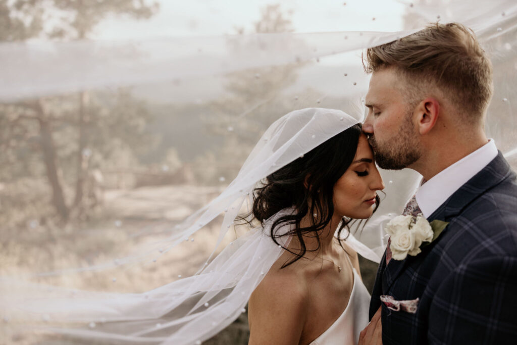 groom kisses brides head under veil during micro wedding in colorado.