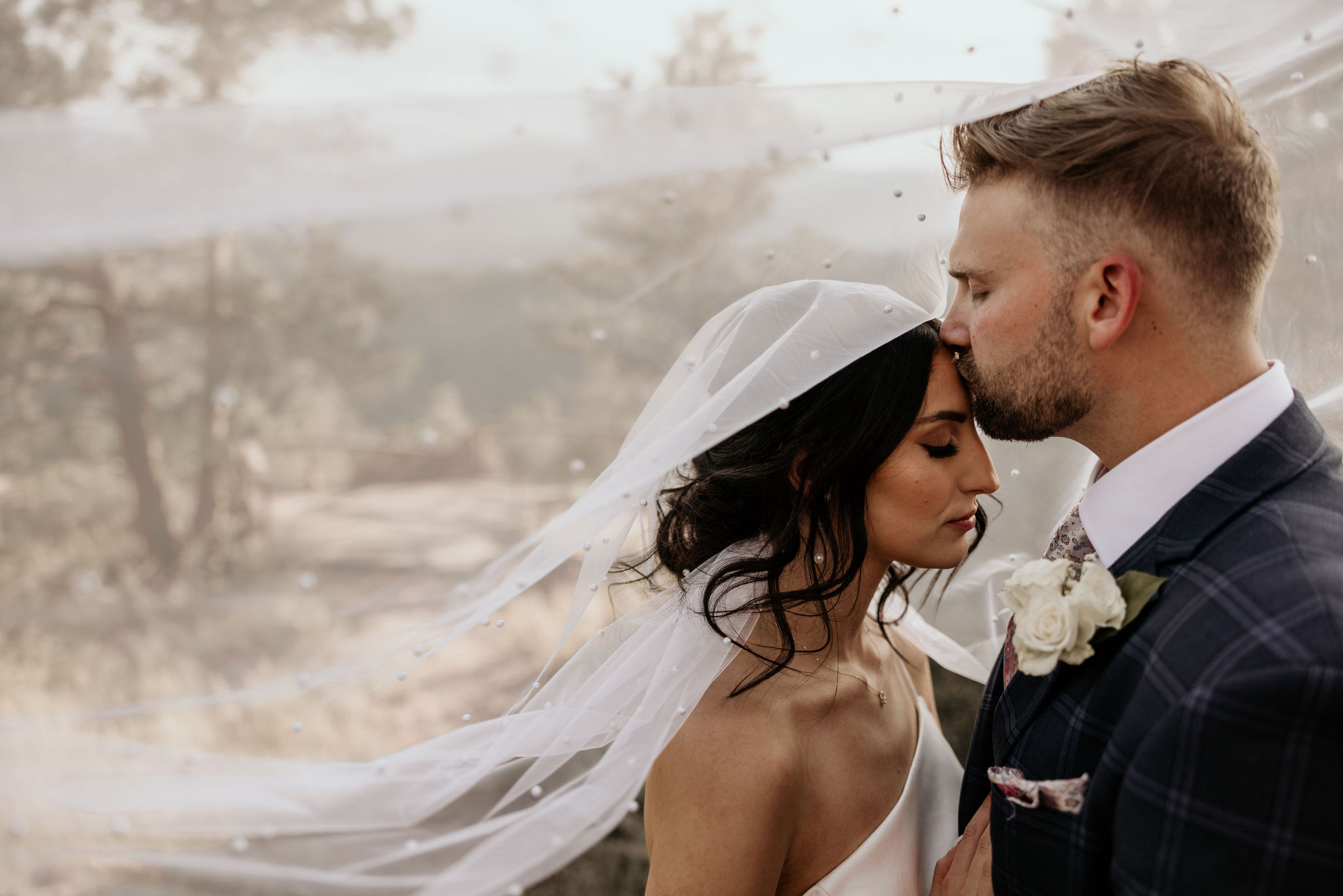 groom kisses brides head under veil during micro wedding in colorado.