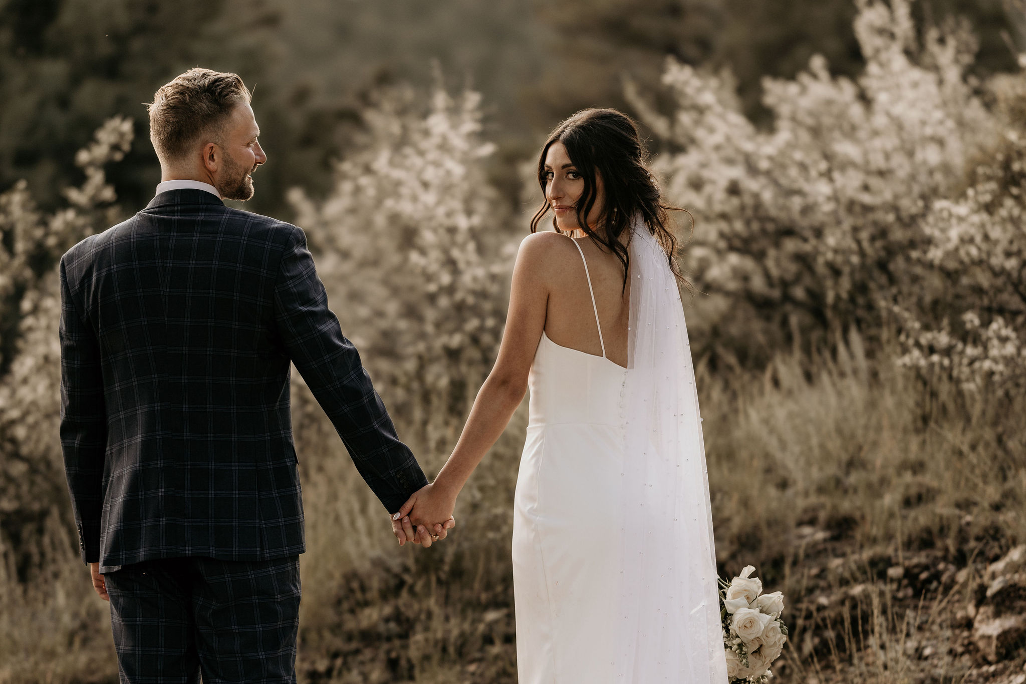 bride and groom holds hands and bride looks back, during wedding portraits in colorado.