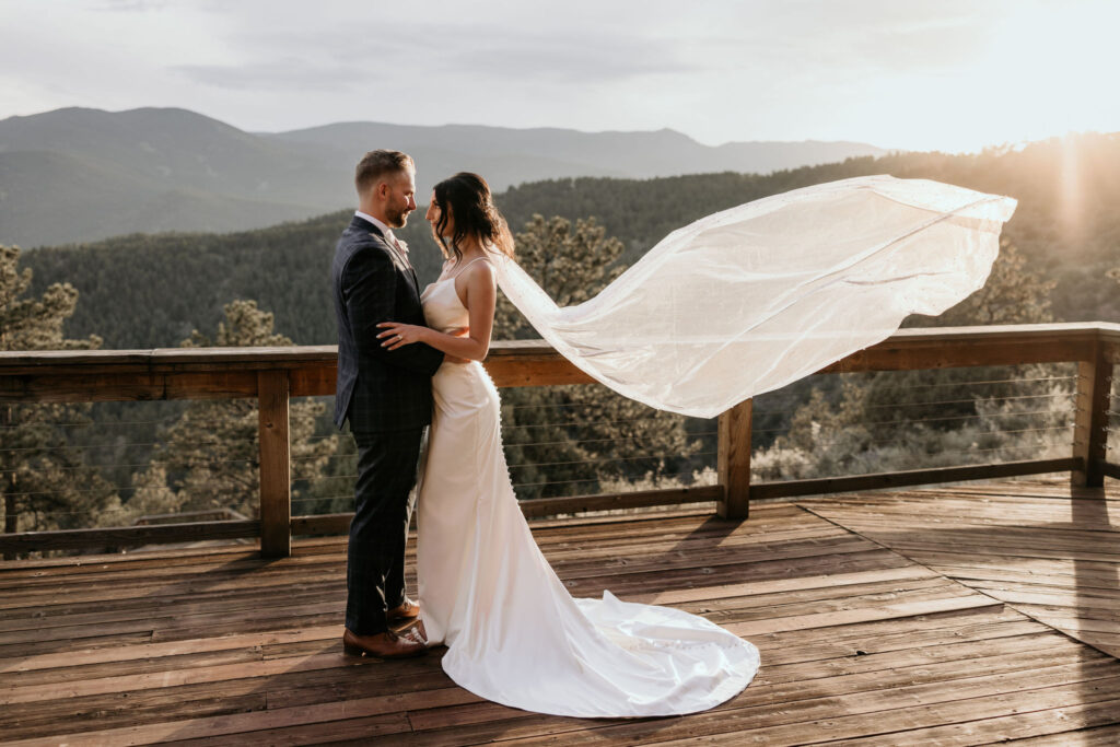 bride and groom out on deck overlooking the mountains, veil in the wind.