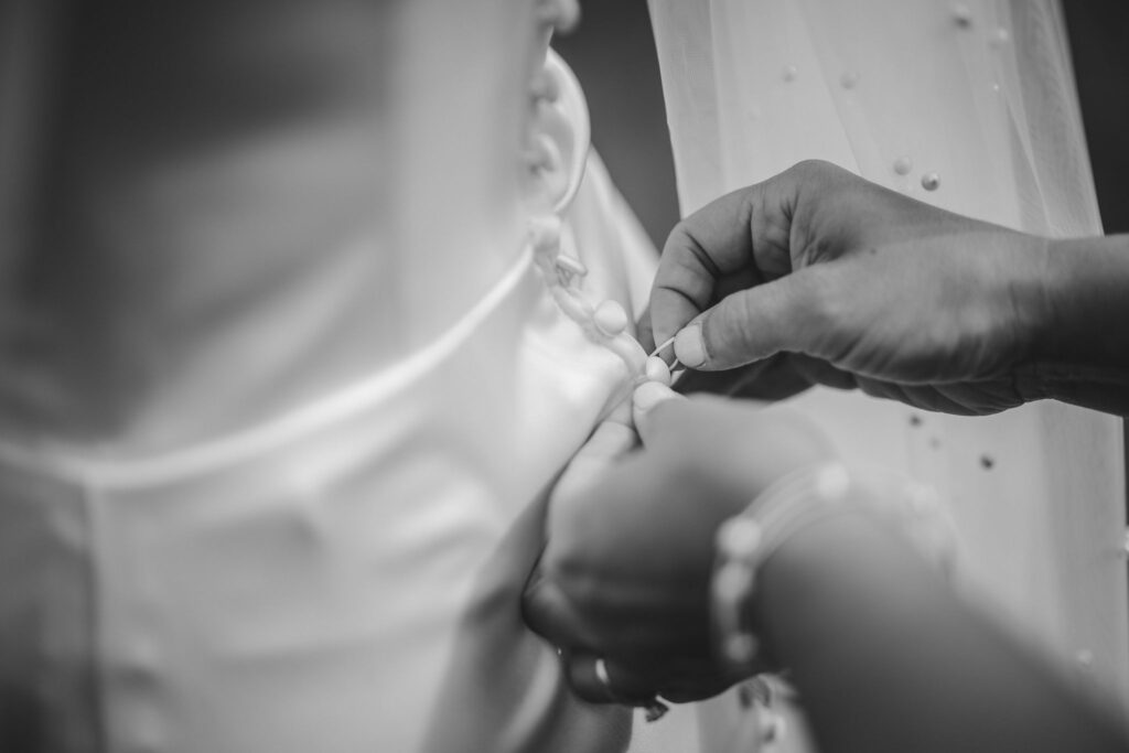 close up image of someone helping the bride button her wedding dress.