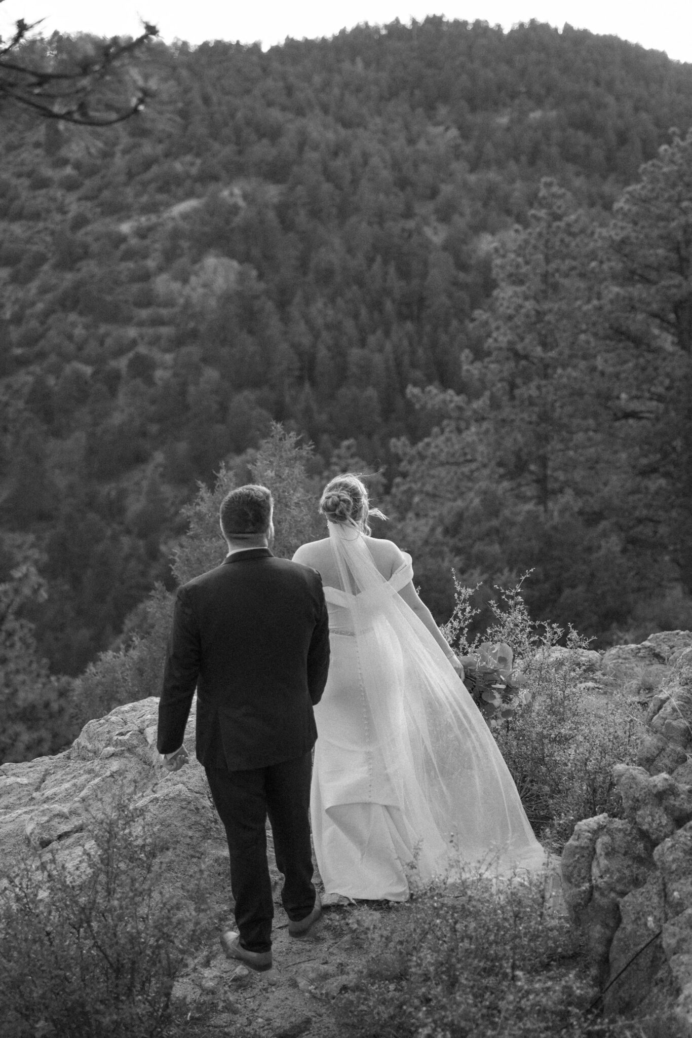 bride and groom stand on the edge of a rocky ledge while they meditate after planning a wedding while grieving