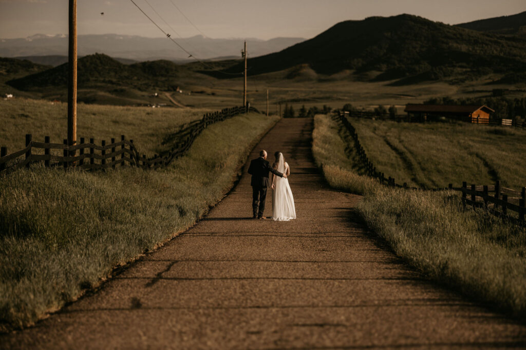 bride and groom walk down dirt road during colorado ranch wedding.