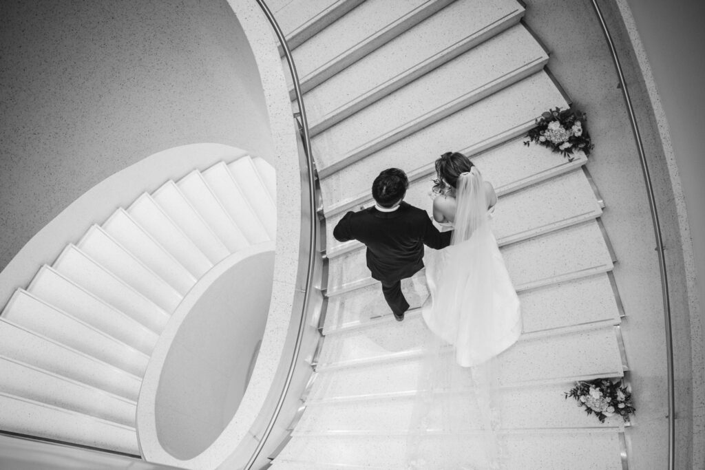 black and white photo of a bride and groom walking down a spiral staircase.