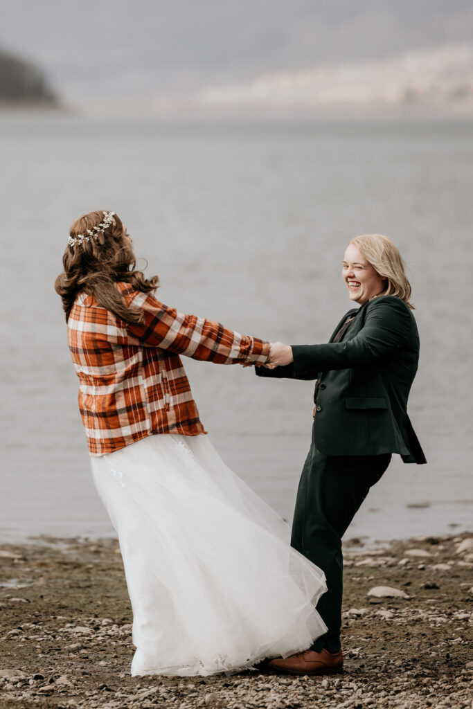 newlywed couple hold hands and twirl along Dillon Reservoir during their LGBTQ+ elopement in colorado.