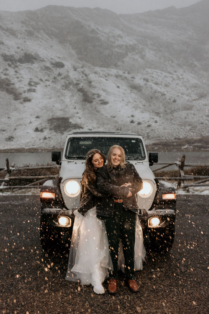 newlywed couple hug in front of jeep with headlights on during snowy elopement photos in colorado.