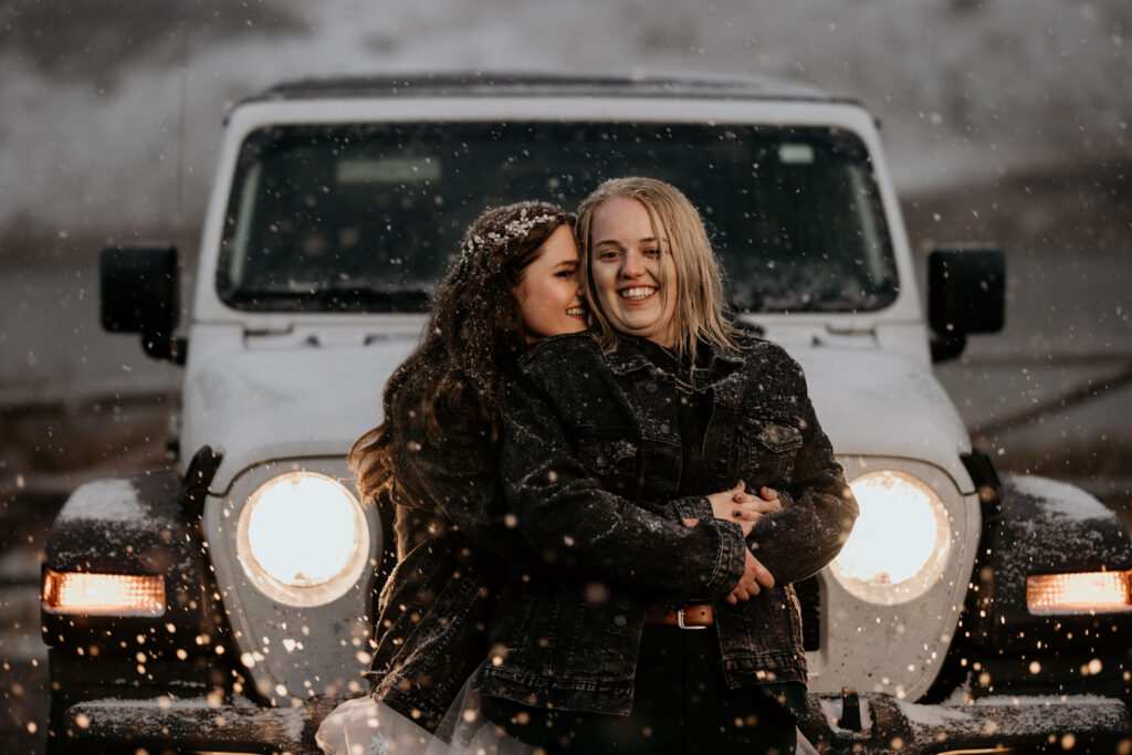 newlywed couple sit on front of jeep and smile during LGBTQ+ elopement portraits.