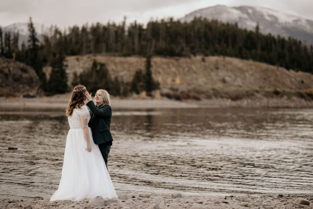 newlywed couple embrace in front of a mountain lake in colorado during their LGBTQ+ elopement.