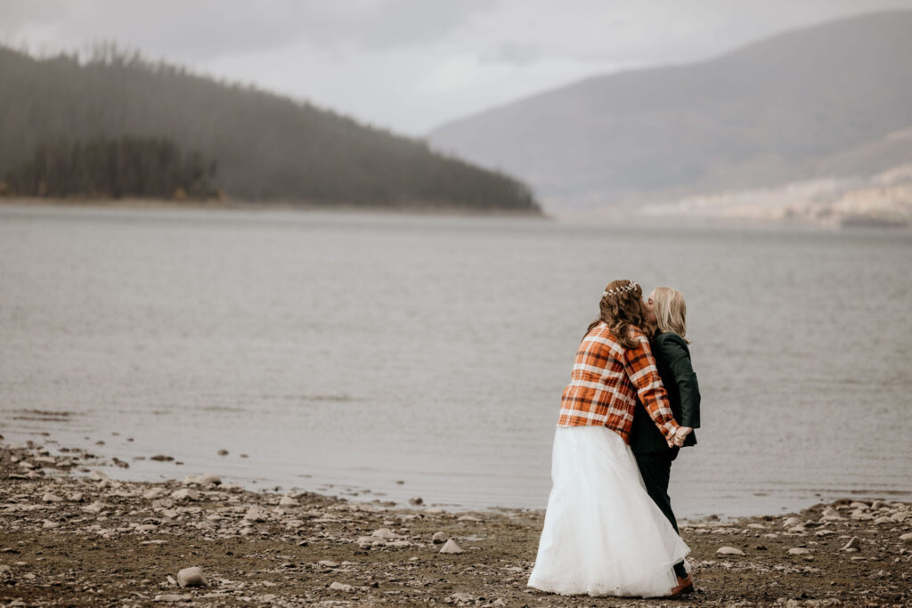 newlywed couple holds hands and kisses in front of Dillon Reservoir for their Breckenridge elopement.