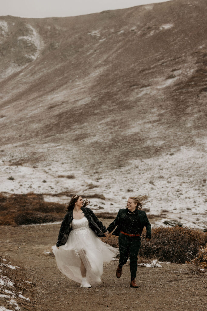 newlywed couple hold hands and run down trail during snowy elopement photos.
