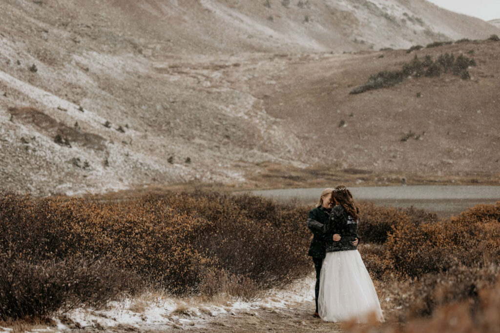 newlywed couple embrace and kiss at Loveland Pass Lake during LGBTQ+ elopement.