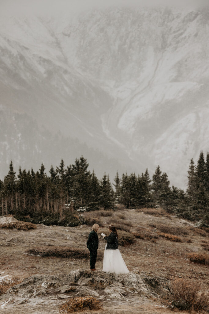 newlywed couple stand on rock with snowy mountains in the background during their breckenridge elopement ceremony.