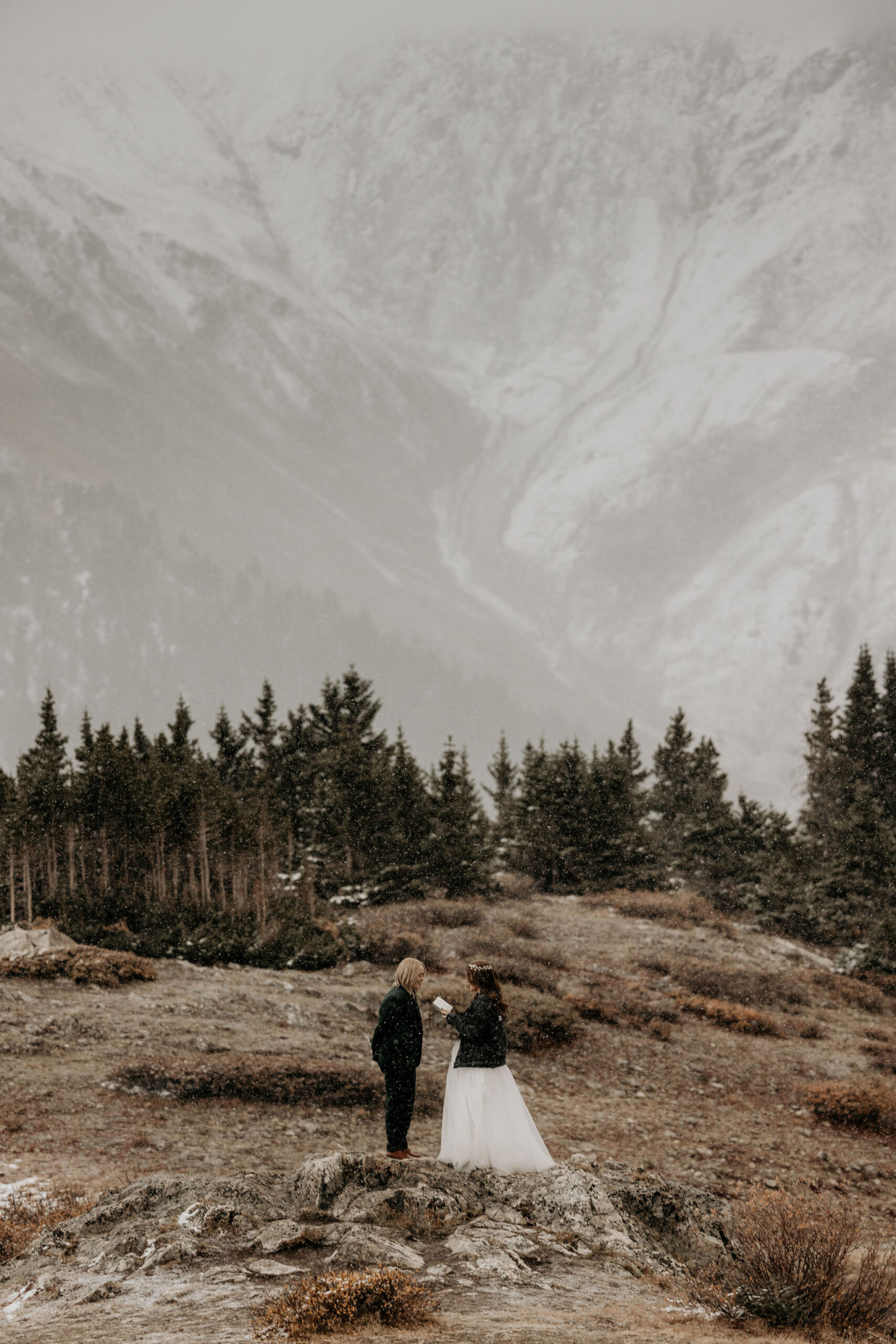 newlywed couple stand on rock with snowy mountains in the background during their simple elopement ceremony.