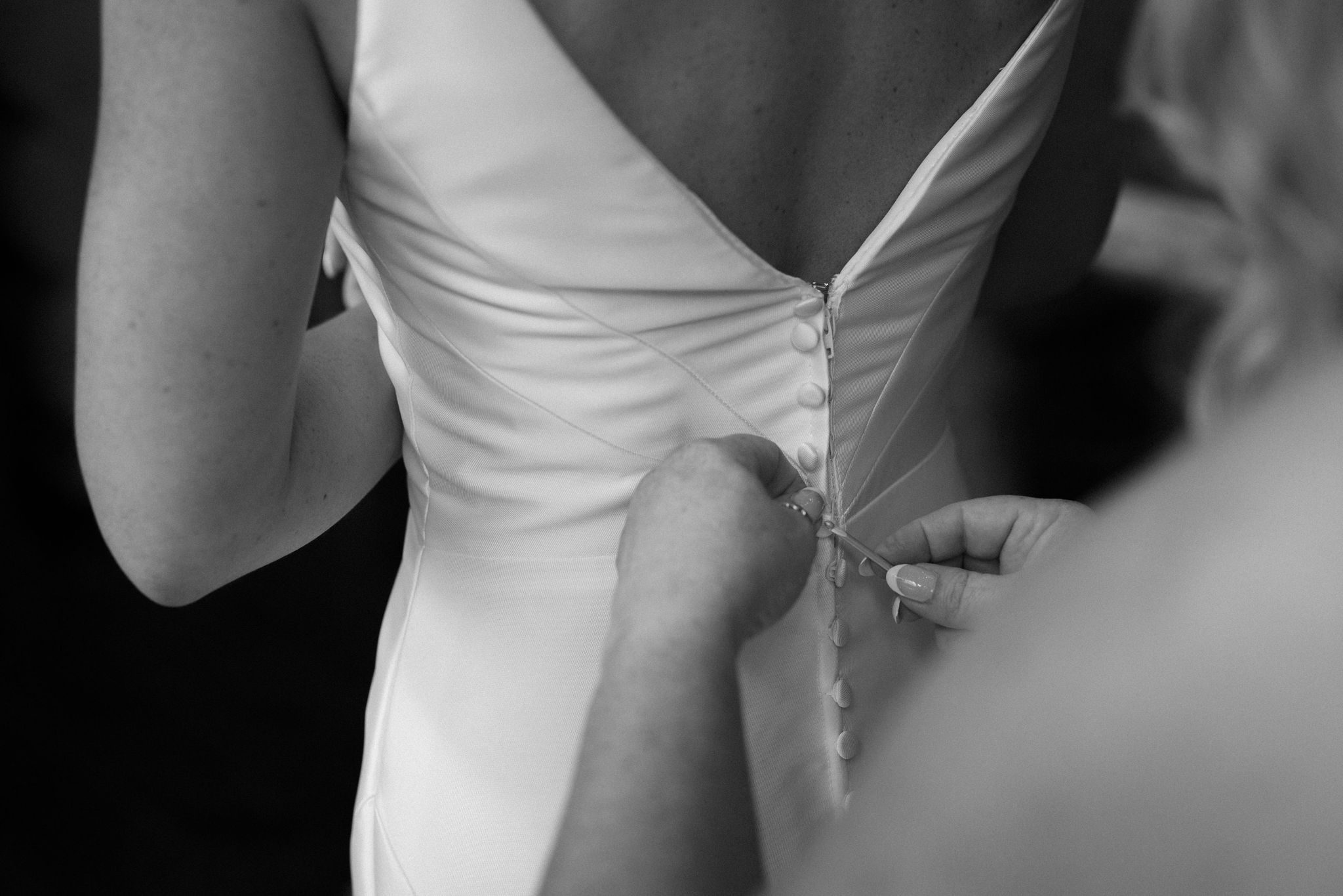 black and white photo of someone helping the bride button the back of her wedding dress after planning a wedding while grieving