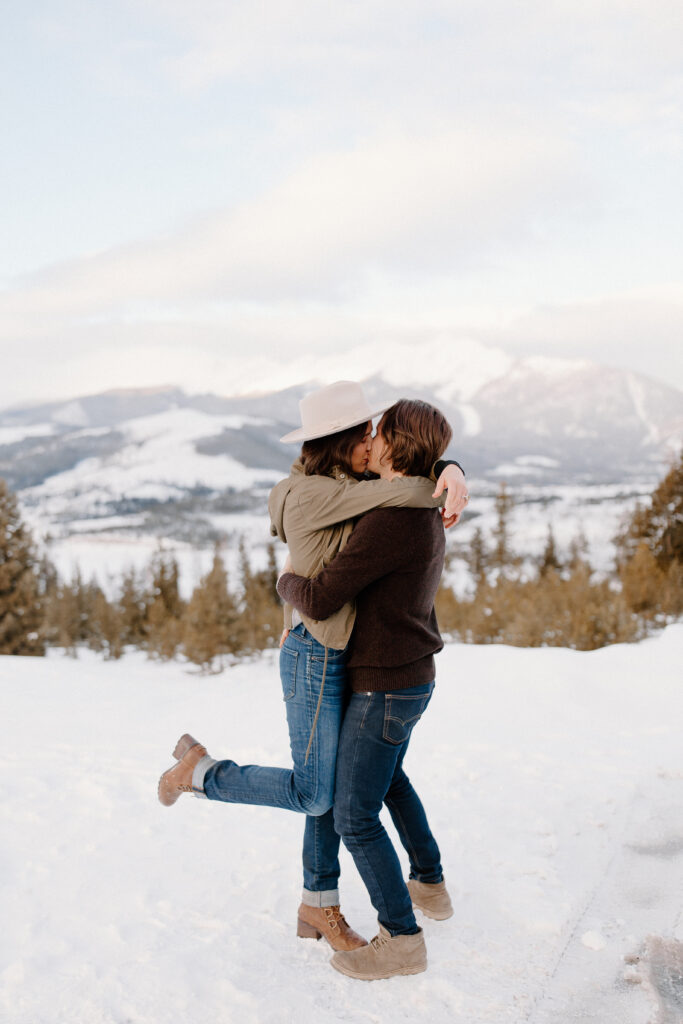 man and woman kiss in front of the colorado mountains during engagement photos.