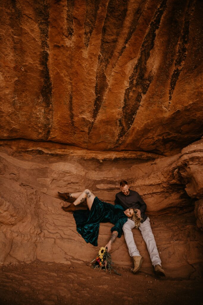 man and woman sit on red rock during colorado engagement photos.