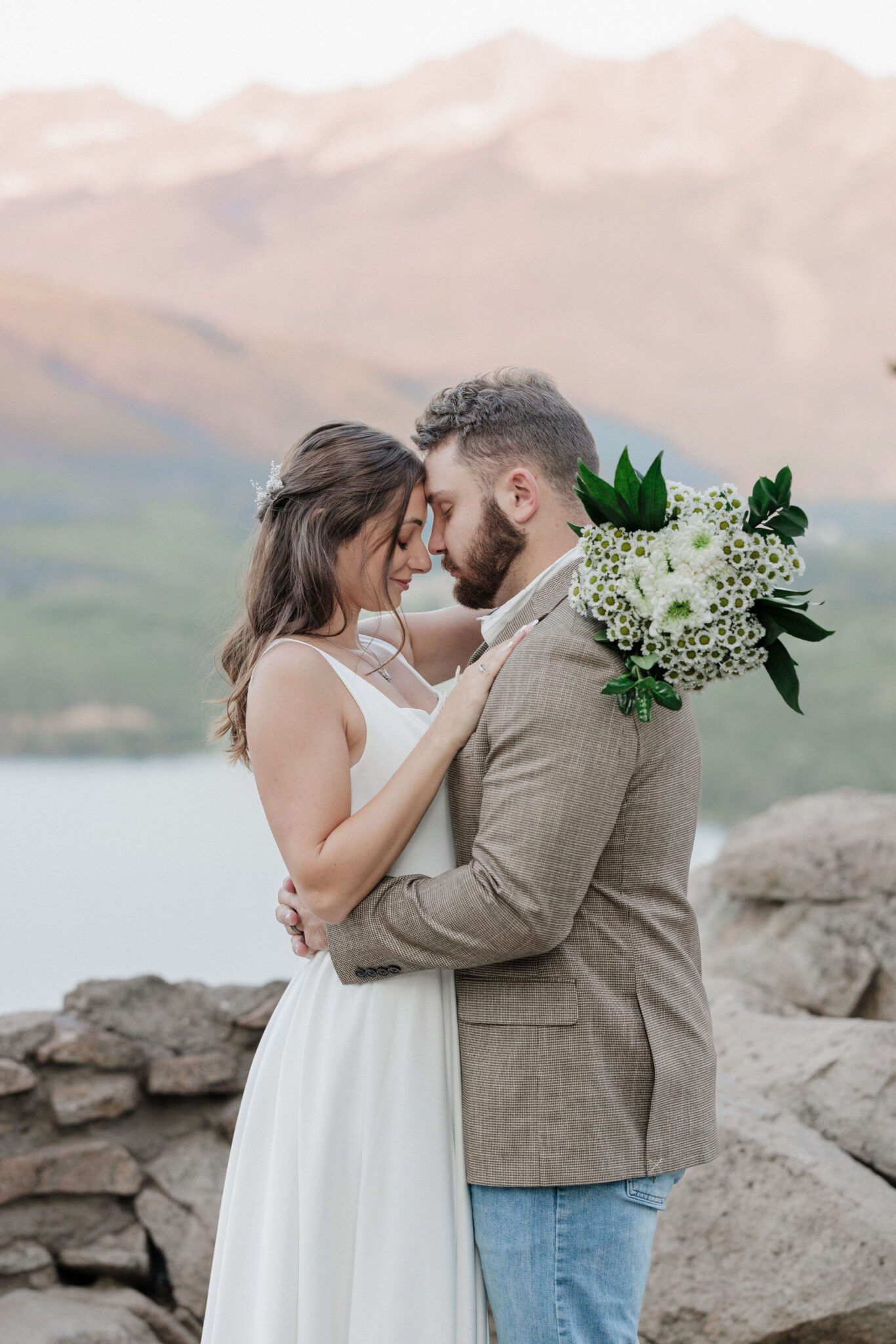 man and woman stand with their heads together in front of the colorado mountains during photo shoot