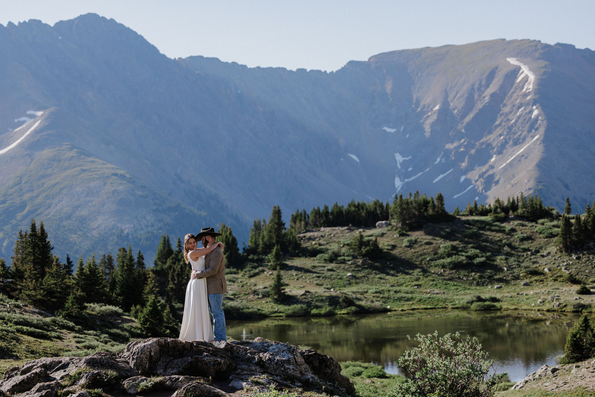 bride and groom stand on rock at pass lake during colorado elopement