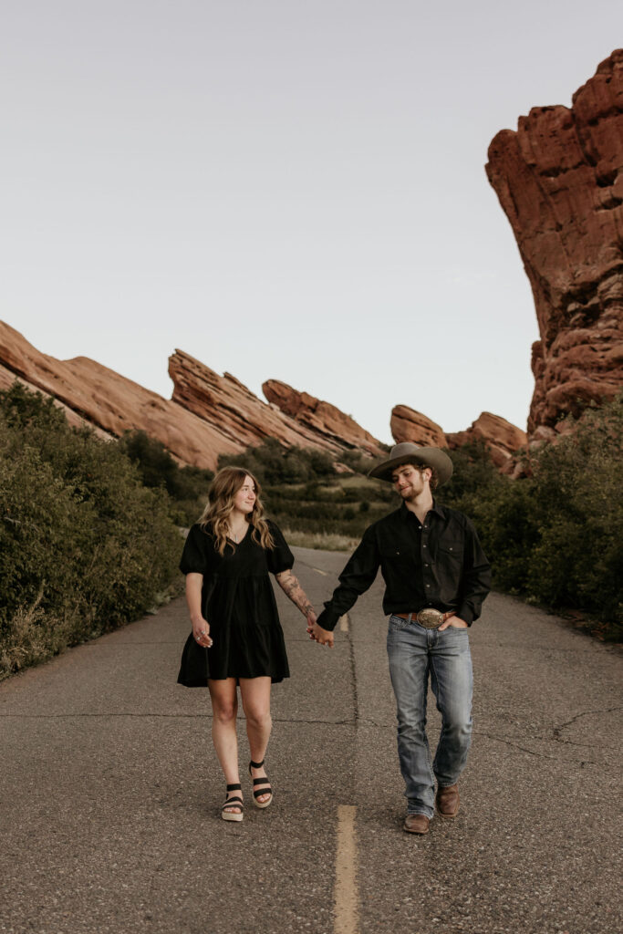 man and woman walk hand in hand at red rocks park & amphitheatre during colorado portrait session.