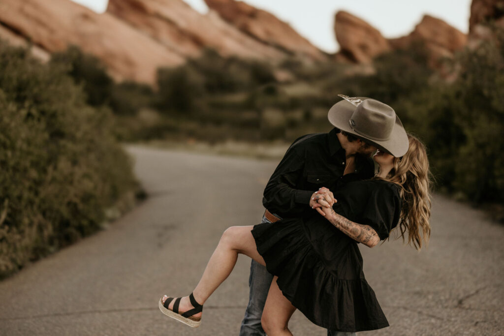 man dips and kisses woman at red rocks park during couple photo shoot.