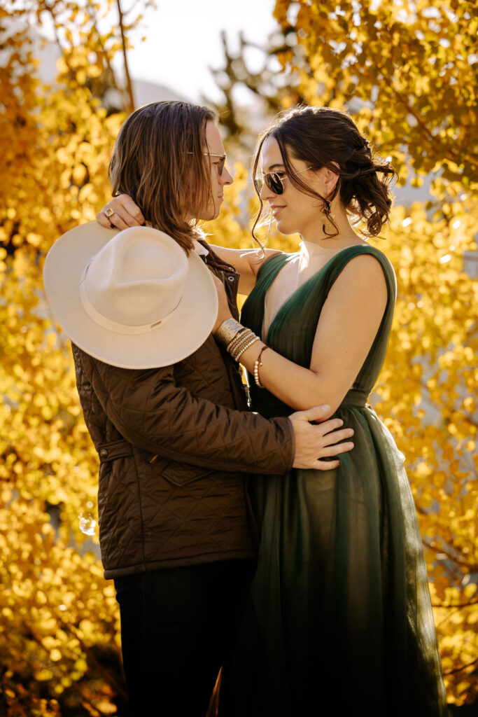 man and woman embrace in front of gold aspens during engagement photos.