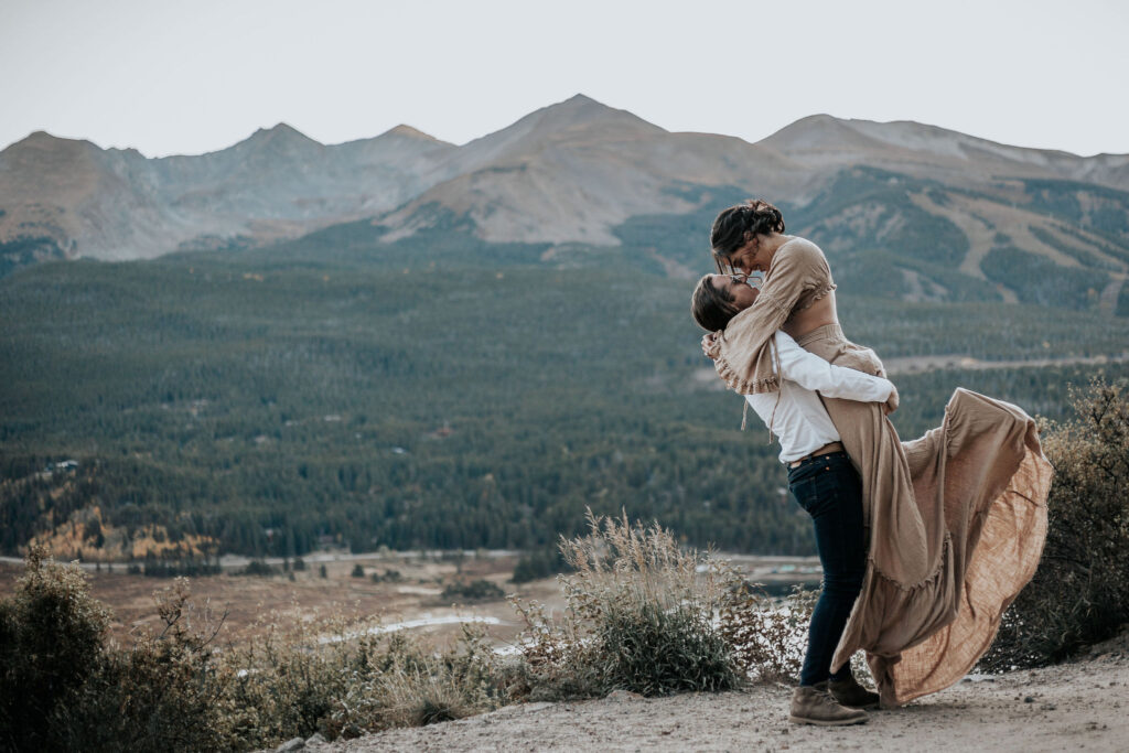 man picks up woman in front of the colorado mountains during portrait session at boreas pass.