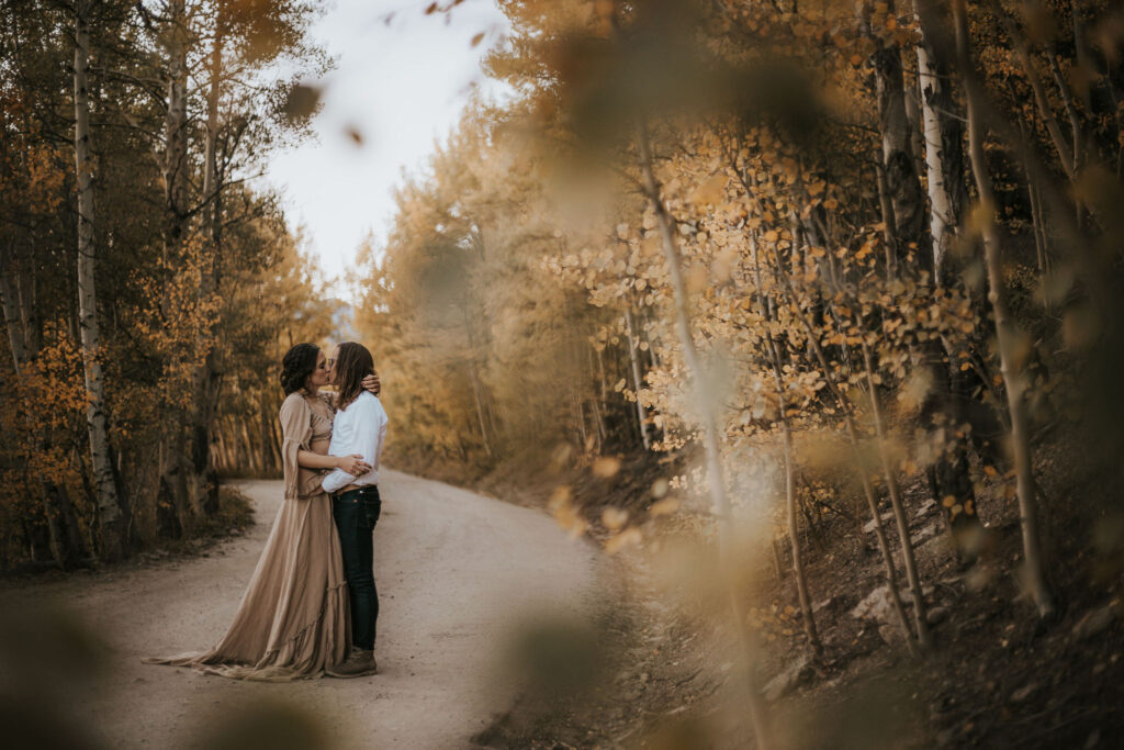 man and woman stand in road lined with aspens during couples portraits in colorado.