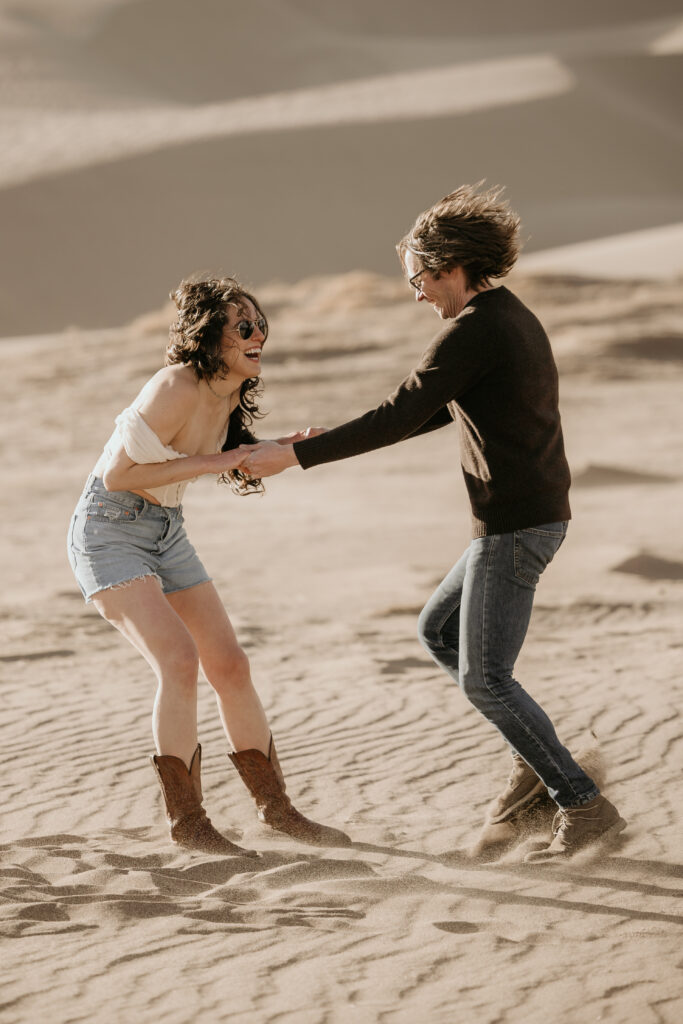 couple plays around and smiles at great sand dunes national park during portrait session.