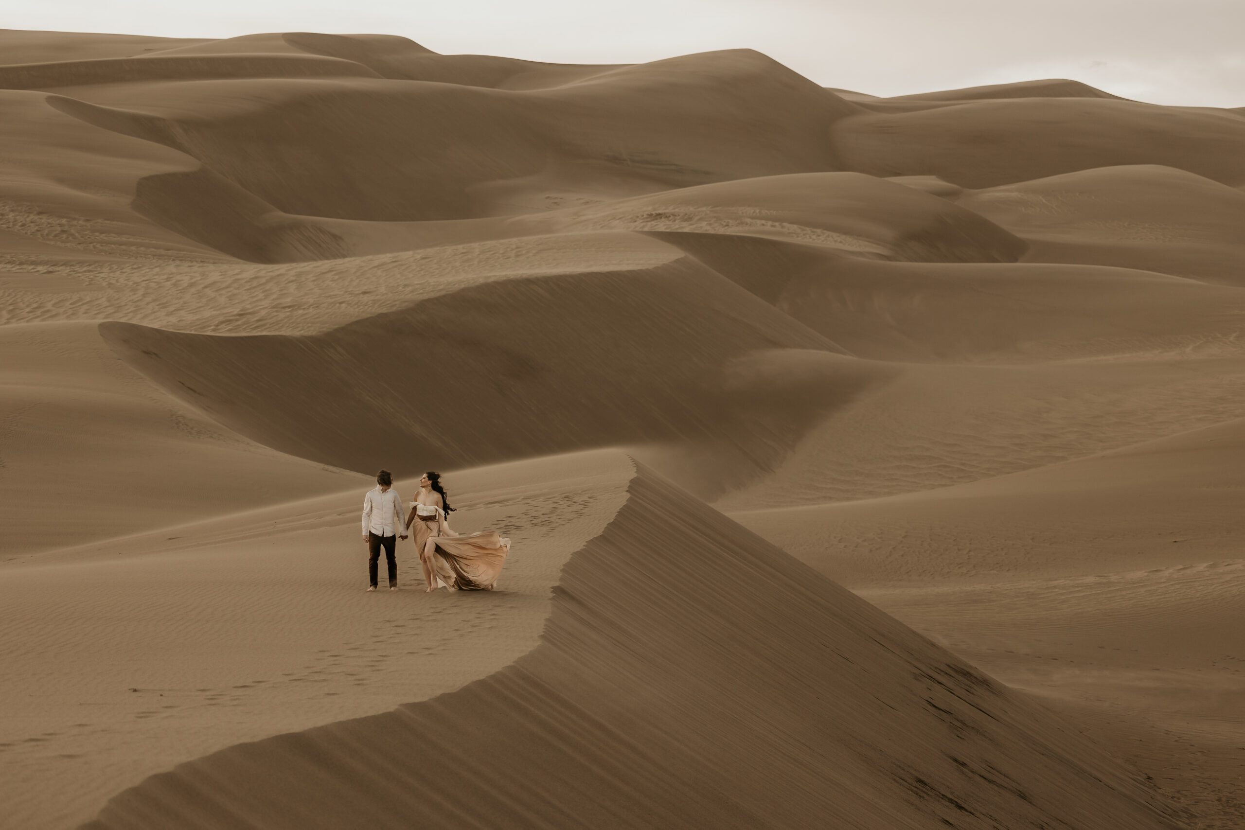 couple walks hand in hand on the sand dunes at great sand dunes national park colorado.